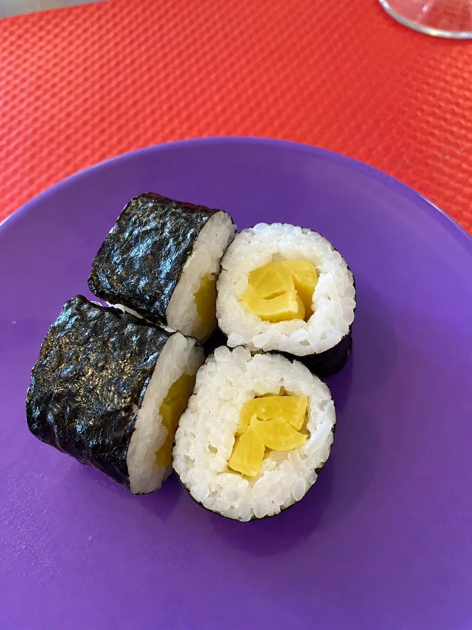 Four pickled-radish maki on a purple plate, red place mat.