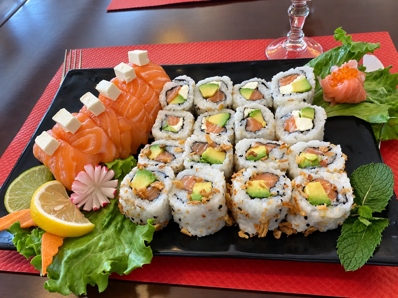 Platter of california rolls and salmon sashimi on a red place mat.